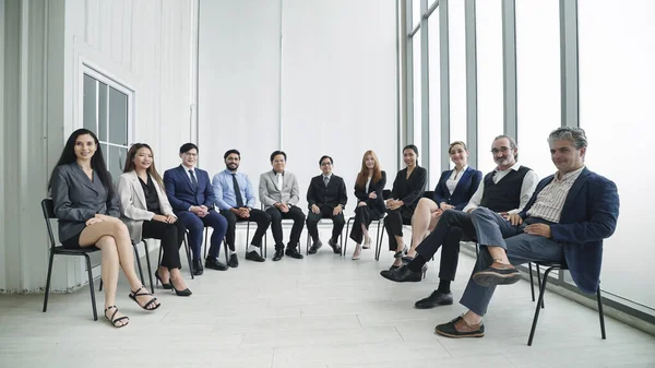 Group of diverse corporate colleagues sitting together in modern office. Successful company with business group of people smiling and looking at camera. Mixed age group of business professionals