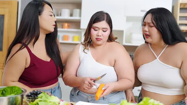 Group of cheerful chubby women friends feeling sad while cooking, preparing salad together in kitchen room. Group of chubby women friends feeling sad while diet. Eating healthy food concept