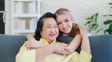 Neşeli Asyalı anne ve küçük kızı kucaklaşıp kameraya bakıyor. Portre seven kız, kameraya gülümseyen orta yaşlı anneye sarılıyor. Aile günü konsepti, anneler günü konsepti.