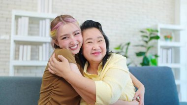 Neşeli Asyalı anne ve küçük kızı kucaklaşıp kameraya bakıyor. Portre seven kız, kameraya gülümseyen orta yaşlı anneye sarılıyor. Aile günü konsepti, anneler günü konsepti.