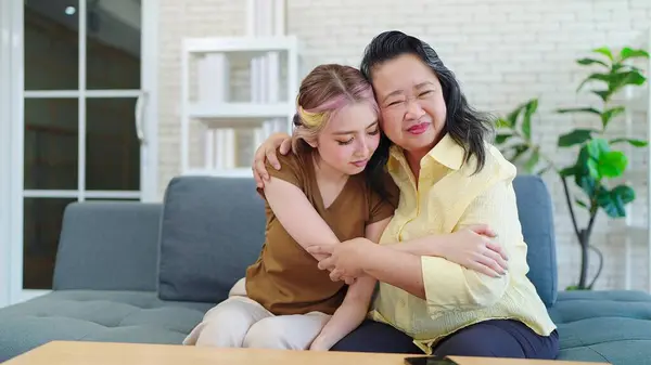 Happy Asian parent mother with young daughter hugging cuddle together while sitting on sofa at home. Young Asian woman and eldery mother spending time together at home. Family day concept