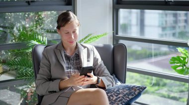 Ofiste otururken akıllı telefondan yazı yazan Kafkasyalı genç bir iş kadını. Mutlu iş kadını sosyal medyada akıllı telefondan arkadaşıyla sohbet ediyor.