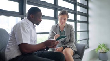 İş adamı ve kadın modern ofiste otururken dijital tablet üzerinde birlikte çalışıyorlar. İki iş adamı ofiste otururken tartışıyor ve tablet kullanıyor