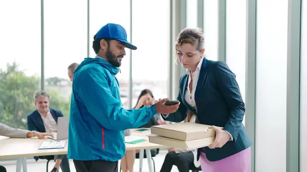 Woman manager taking pizza box from food delivery man for enjoy lunch together with colleagues in meeting room at office.Women manager orders food online to team. Delivery food concept