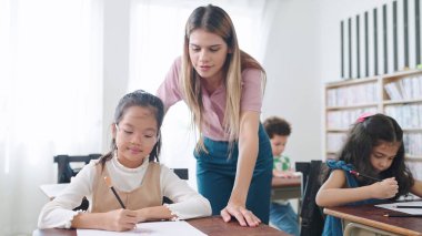Bayan öğretmen sınıftaki çocuklara yardım ediyor. İlköğretim öğretmeni sınıftaki öğrencilere ders veriyor. Eğitim bilgisi kavramı