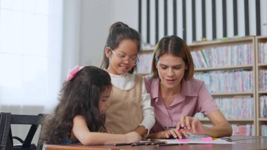 Bayan öğretmen sınıftaki çocuklara yardım ediyor. İlköğretim öğretmeni sınıftaki öğrencilere ders veriyor. Eğitim bilgisi kavramı