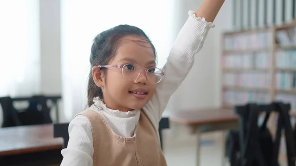 Active excellent Asian student schoolgirl in glasses raising hands up answer the questions in classroom at school. Portrait of children studying in classroom at the school. Children learning concept