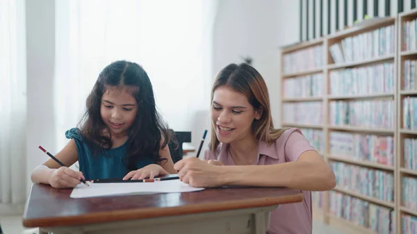 Caucasian woman teacher helping schoolgirl to finish a lesson. Beautiful woman teacher teaching student schoolgirl education answer on notebook in classroom at school. Education concept