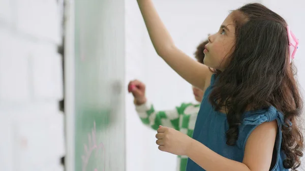 幼稚園のアジアの少女は 学校の教室でチョークボードを書いたり描いたりします 小さな女の子は 教室教育と学習の概念で緑のボードに書いています — ストック写真