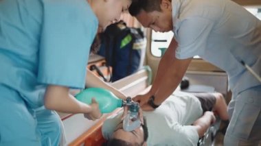 Sağlık görevlisi acil durum arabasındaki sedyelerle yaralı adama kalp masajı yapıyor. Tıbbi asistan nefes almak için maske kullanıyor.