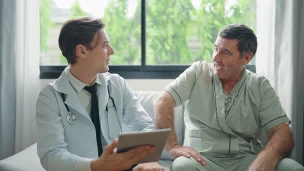 デジタルタブレットを使用して若い医師は治療後の患者に症状を説明するか 病院の老人患者と話す — ストック動画