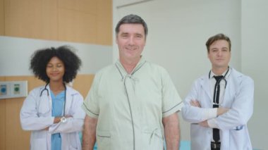 Tıbbi yardım alan ve kameraya bakan gülümseyen hasta hastane odasında bekleyen tıbbi çeşitlilik ekibi. Yaşlılar sağlık hizmeti kavramı.