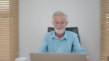 Evde dizüstü bilgisayarla çalışırken gülümseyen yaşlı, mutlu beyaz iş adamı..