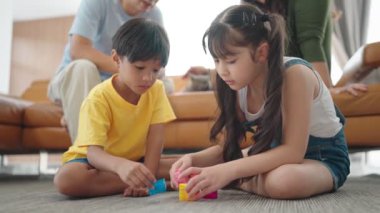 Asyalı bir ailenin tatilde evdeki oturma odasında birlikte zaman geçirmesi. Aktivite ilişkisi. Küçük iki çocuk, kız ve oğlan farklı renklerde oyuncaklarla oynuyorlar..