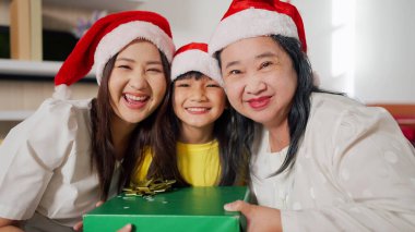 Üç nesildir Noel Baba şapkalı Asyalı kadınlar ellerinde hediye kutusuyla kameraya gülümsüyorlar. Mutlu Noeller ve mutlu tatiller. Aile, kış tatili ve insanlar konsepti.