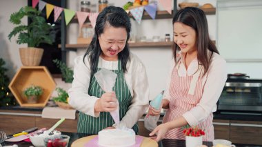 Mutlu Asyalı yaşlı anne ve küçük kızı birlikte pastaya krema sıkıyor. Anne ve kızı Noel günü için pasta yapıyorlar. Noel pastası süslenmiş. Bayram kutlamaları.