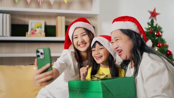 Happy family at home during christmas eve day enjoy a video phone call with parents. Happy Grandmother, mother and little daughter having video call with family in Christmas day