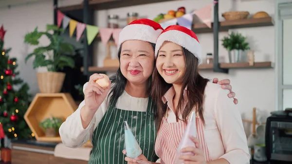 Happy asian elderly mother and young daughter in apron smiling to camera. Cheerful mother and young daughter in kitchen room at home. Family and cooking concept