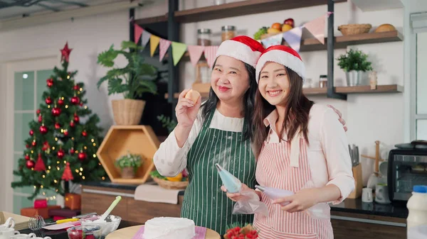 Happy asian elderly mother and young daughter in apron smiling to camera. Cheerful mother and young daughter in kitchen room at home. Family and cooking concept