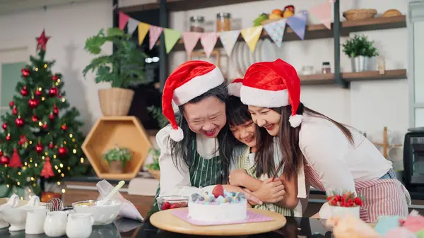 Happy Grandmother, mother and little daughter decorated cake together for Christmas Eve. Three generations Asian women making cake for Christmas day. Christmas cake decorated. Festive holiday