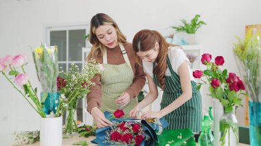 Çiçekçi dükkanının Asyalı kadın sahibi stajyere çiçekçide nasıl kompozisyon yapılacağını öğretiyor. Çiçekleri buketlere yerleştiren iki çiçekçi. Küçük işletme kavramı