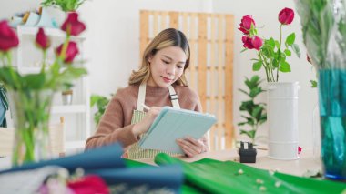 Küçük işletme konsepti. Çiçekçide sipariş üzerine tablet yazan Asyalı genç bir çiçekçi. Çiçekçi ya da çiçekçi kadın tablet kullanıyor, çiçekçide sipariş alıyor.