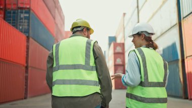 Güvenlik üniformalı iki endüstri mühendisinin konteynır deposunda yürürken yan yana çalışmalarının görüntüsü. Sanayi işçileri konteynır kutusunu fabrikadan kargo gemisine kontrol ediyor.
