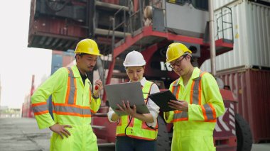 Endüstriyel bir depoda çalışan, dizüstü bilgisayar ve tablet üzerinde çalışan ve kargo konteynerinde birlikte konuşan çalışkan işçiler. Takım çalışması konsepti