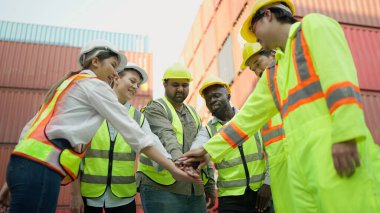 Mühendis ve ustabaşı takım halinde zırhlı ve güvenlik üniformalı bir şekilde konteyner deposu nakliye limanında el ele tutuşuyorlar. Başarılı takım çalışması konsepti. Kargo sevkiyatı, Lojistik konsept