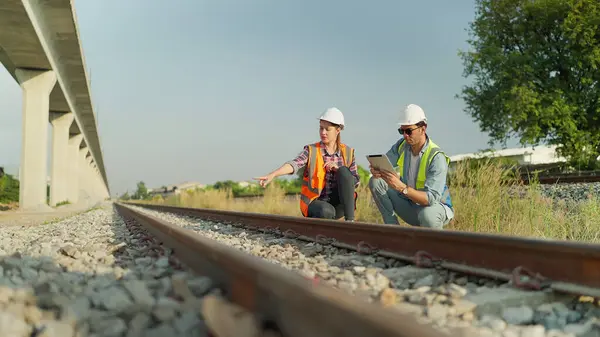 Two engineers in safety uniform and helmet using tablet discussion and inspection construction process railway. Two engineer working on railway together. Teamwork concept