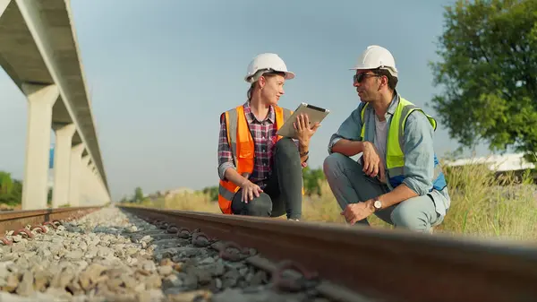 Two engineers in safety uniform and helmet using tablet discussion and inspection construction process railway. Two engineer working on railway together. Teamwork concept
