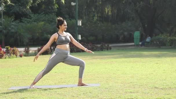 公園でVirabhadrasana 戦士ポーズ ヨガをやっているスポーティーでフィット女性のビデオ — ストック動画