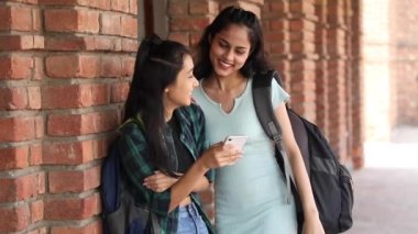 Video of two young girl friends smiling while watching videos on a smartphone and pointing at the screen.