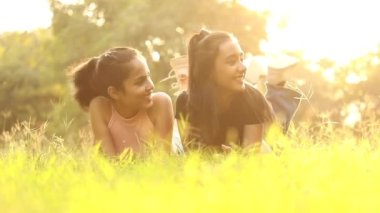 Two happy Indian young girls are lying on green grass in this video.