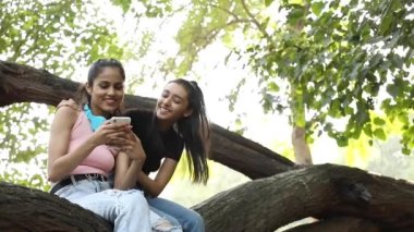 Video of an Indian female friends smiling while scrolling through their phone.