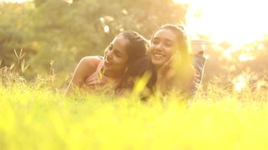 Video of two beautiful girls lying on green grass and having fun in a park.