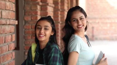 Video of two young girl friends standing together on a university campus and looking at the camera.