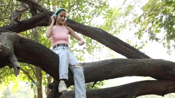 Видеоклип Молодой Индийской Девушки Которая Слушает Музыку Наушниках Сидя Стволе — стоковое видео