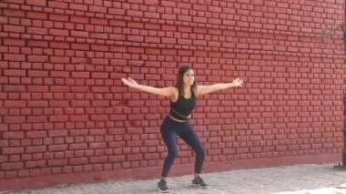 Video of Indian slim woman doing balancing squat exercise standing in front of red brick wall.