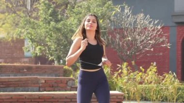 Video footage of Indian woman performing March in place workout standing in front of red brick wall.