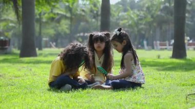 Güneşli bir günde parkta elinde büyüteçle çiçeğe bakan meraklı çocukların videosu.