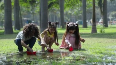 Parkta renkli kağıt teknelerle oynayan üç çocuğun video klibi.
