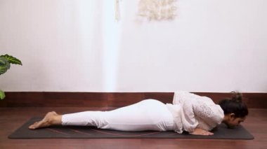 Beyaz elbiseli bir kadının sırt ağrısı için Bhujangasana 'yı sahnelediği video kaset.