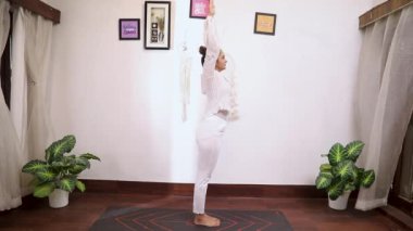  Beyaz elbiseli Hintli bir kadının Hastottanasana yoga pozu verdiği video.