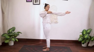  Beyaz elbiseli Hintli bir kadının katihakrasana yoga pozu verdiği bir video.