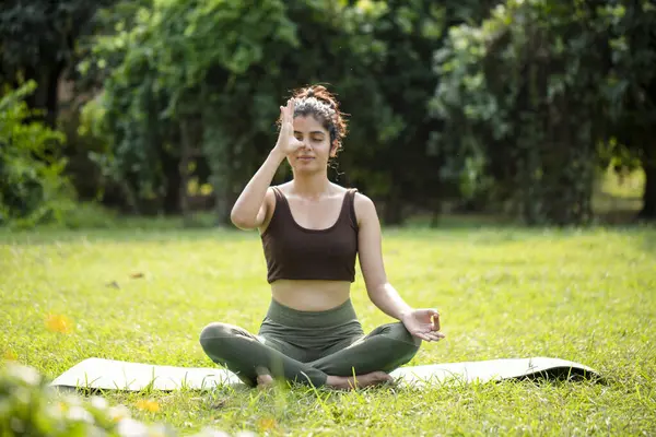 Büyüleyici kadın gözlerini kapatıyor parkta anuloma pranayama egzersizi yapıyor.