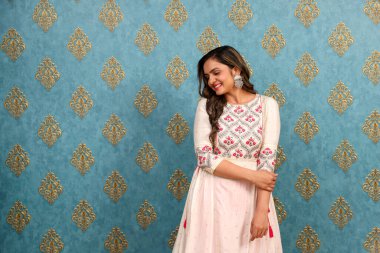 Hintli gibi giyinmiş utangaç bir kadın duvara karşı poz verirken utangaç bir şekilde gülümsüyor.