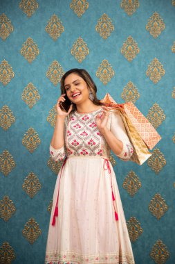 Geleneksel giysiler içinde bir moda kadını cep telefonuyla konuşurken alışveriş torbalarıyla poz veriyor.