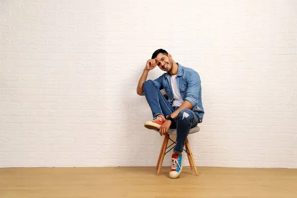 Kot gömlek giyen mutlu bir adam kameranın önünde poz verirken sandalyede oturuyor.