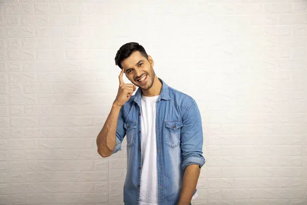 Beyaz arka planda dikilirken kafasında parmak olan yakışıklı bir adam.